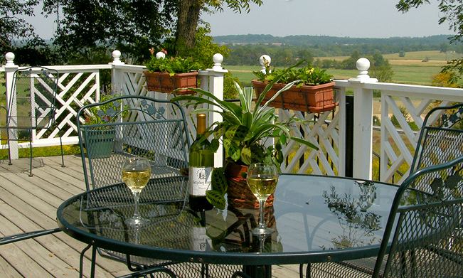 The wooden deck with a glass table overlooking battlefield meadows and distant hills