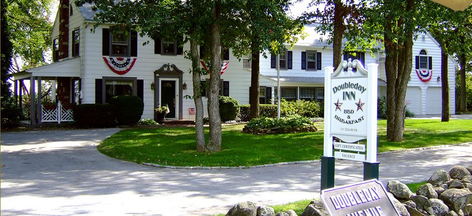 The white two story Doubleday Inn house with blue shutters and the inn sign by the road