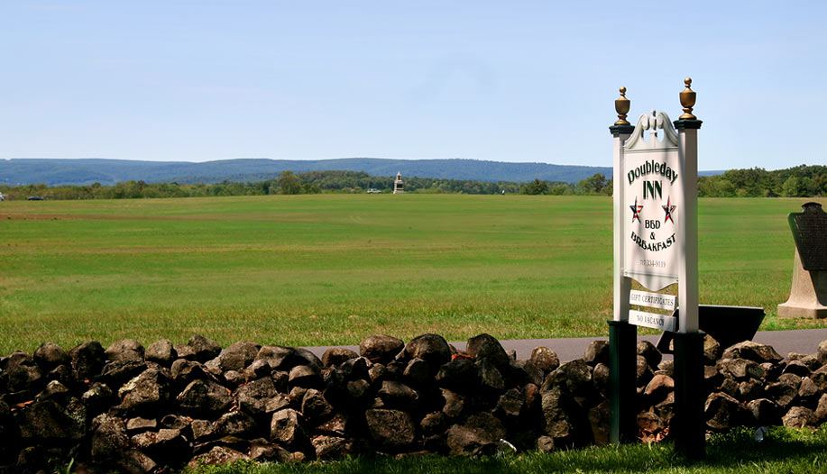 Battlefield meadow and stone wall with the white Doubleday Inn bed and breakfast sign, a distant monument on the horizon
